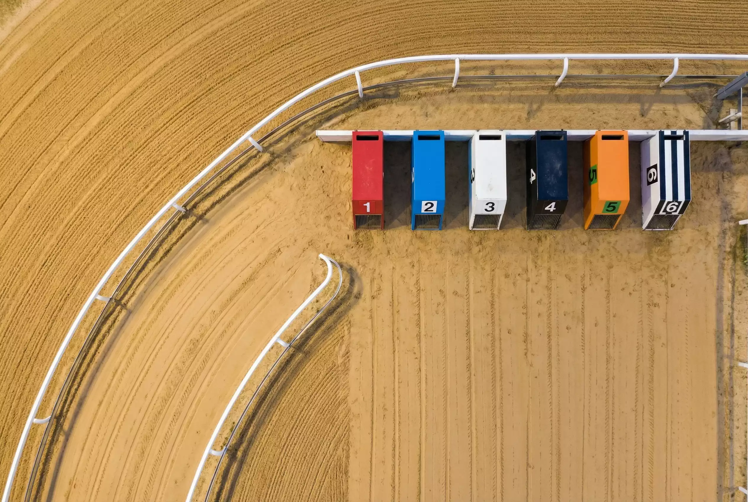 Overhead view of a greyhound racing track showing six numbered starting traps and the first bend on a sand oval circuit